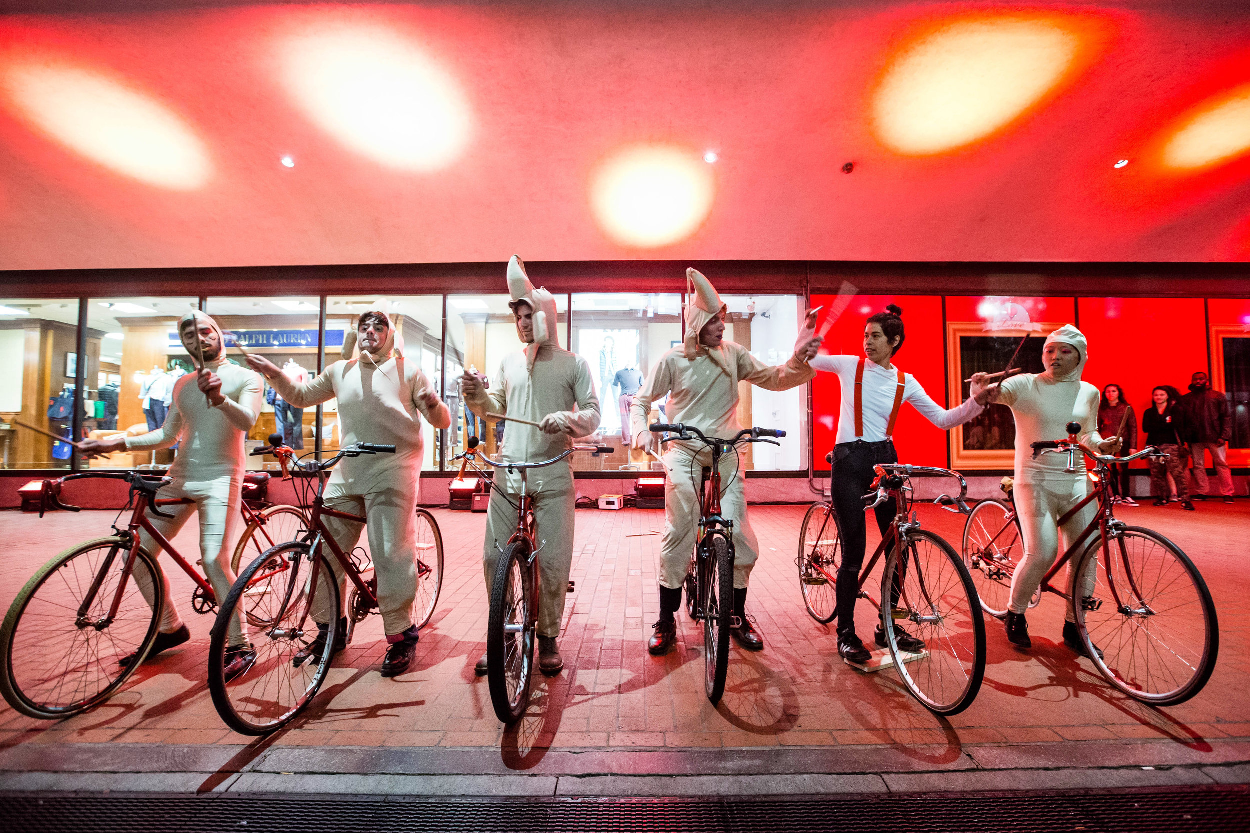 a group of people wearing light clothing and holding drumsticks while sitting on bicycles