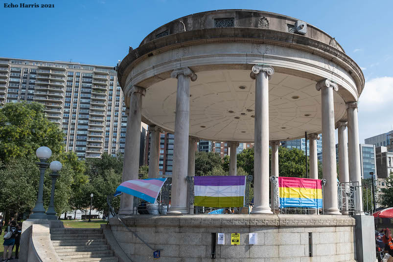 Picture of the Boston Common Parkman Bandstand. Attatched to the banisters are several pride flags including the Transgender Pride Flag, the Pansexual Pride Flag, and the Genderqueer Pride Flag.